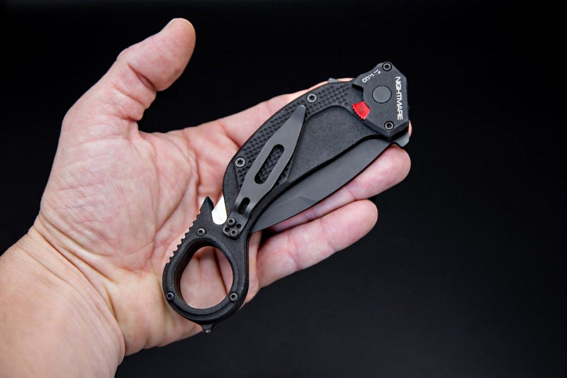Black folding knife held in a hand against a black background